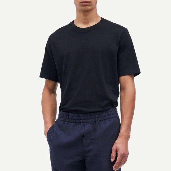 Man wearing a black t-shirt and navy shorts on a white background