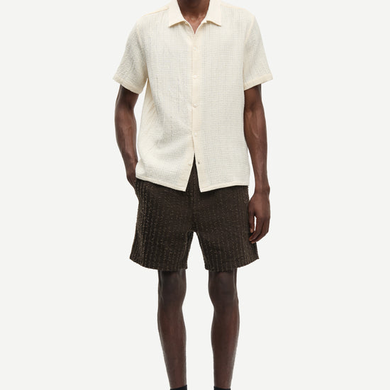 Man wearing a cream short-sleeve shirt and brown shorts on a white background