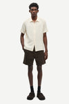 Man wearing a cream short-sleeve shirt and brown shorts on a white background