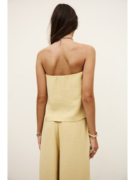 Woman wearing a strapless yellow top and high-waisted pants on a plain background