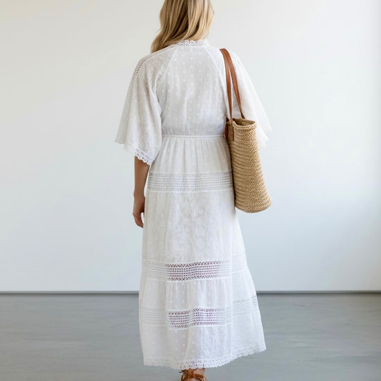 Woman in a white dress holding a woven bag against a plain background