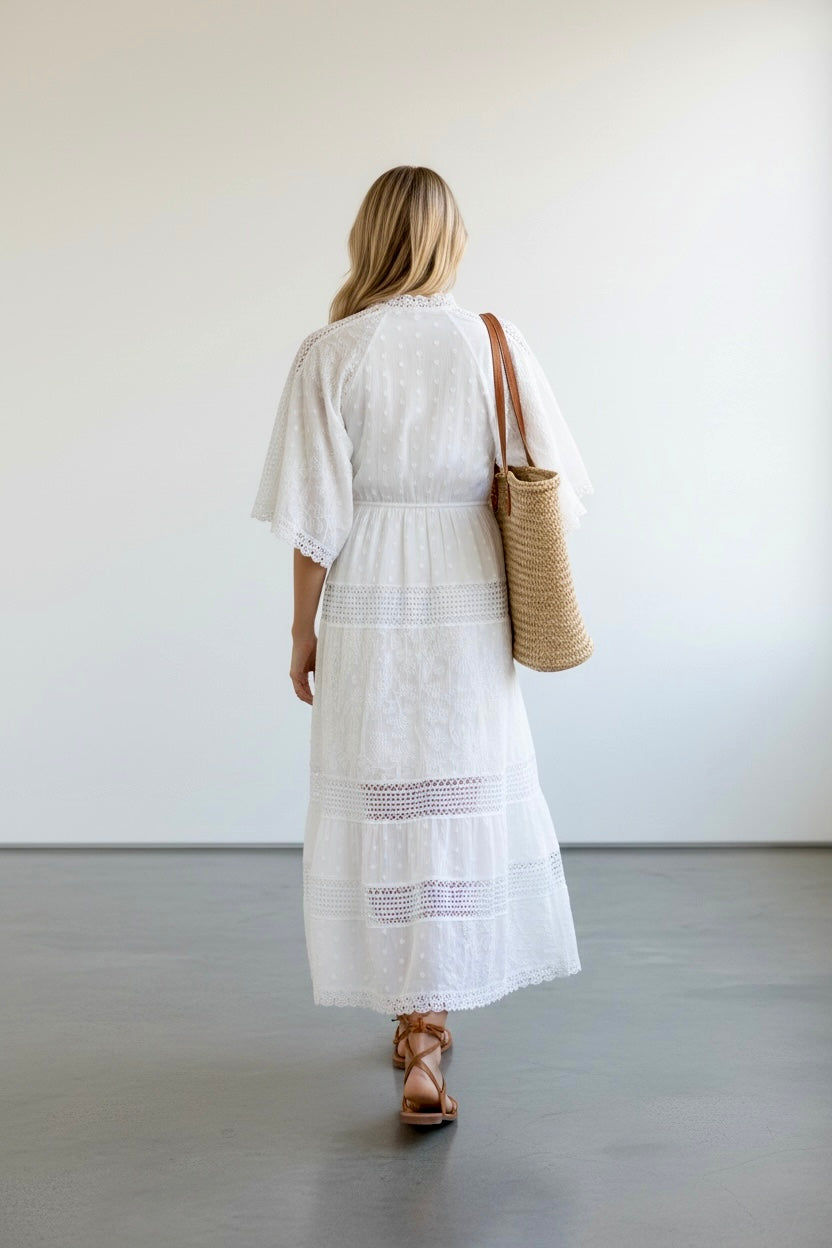 Woman in a white dress holding a woven bag against a plain background
