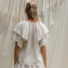 Woman wearing a white lace top in front of sheer curtains