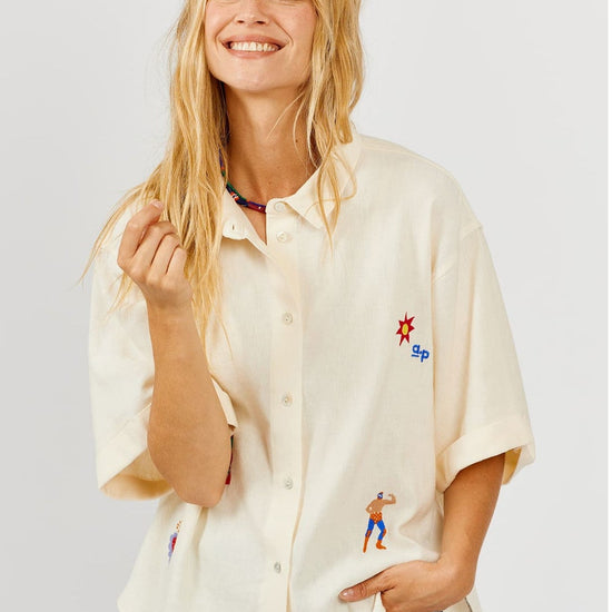 Woman wearing a cream-colored shirt with embroidered designs on a light gray background
