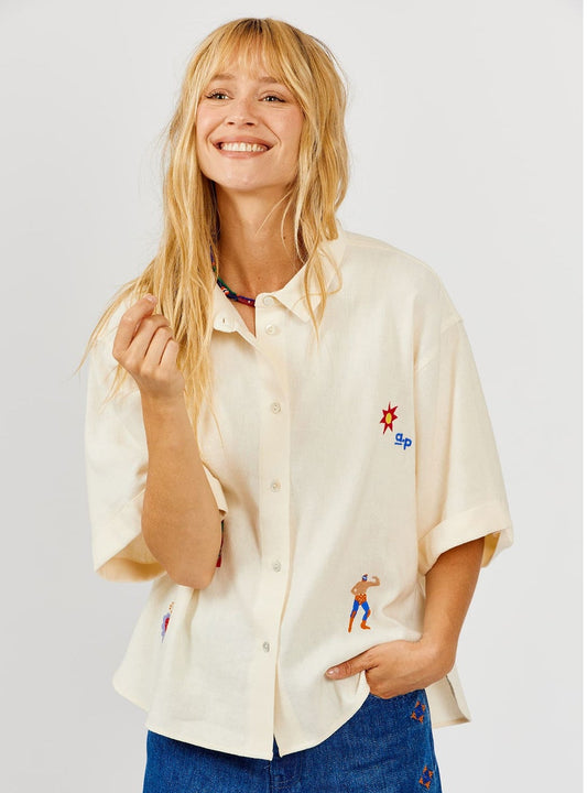 Woman wearing a cream-colored shirt with embroidered designs on a light gray background