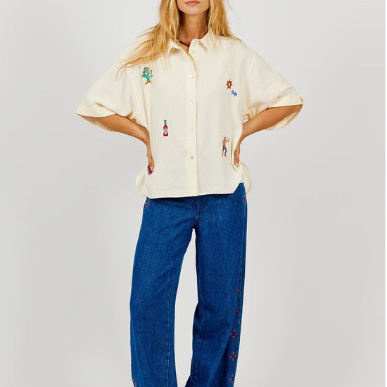 Person wearing a cream-colored shirt with colorful designs and blue jeans on a white background