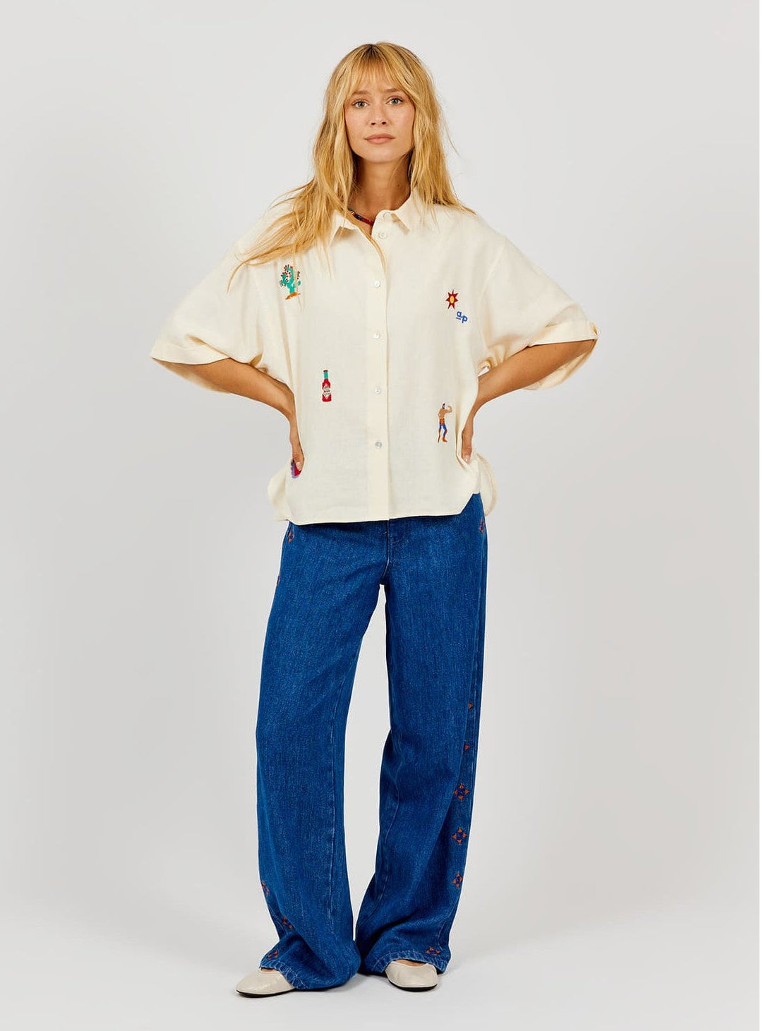 Person wearing a cream-colored shirt with colorful designs and blue jeans on a white background