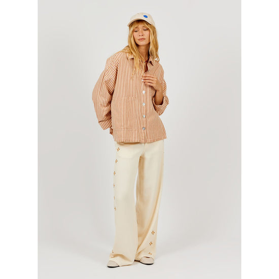 full shot of model wearing a striped shirt and loose fitting trousers on a plain background 