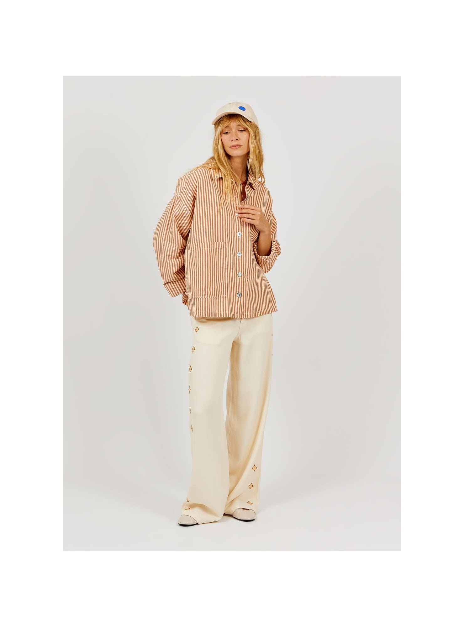 full shot of model wearing a striped shirt and loose fitting trousers on a plain background 