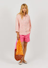 Woman wearing a pink shirt and shorts holding a colorful bag on a white background