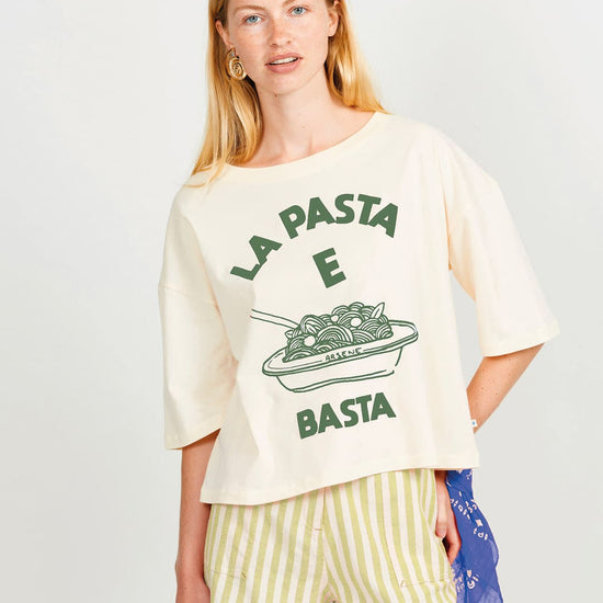 Woman wearing a cream t-shirt with green text and graphics, paired with striped shorts on a white background.