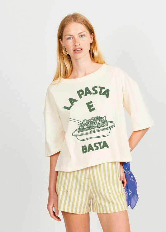 Woman wearing a cream t-shirt with green text and graphics, paired with striped shorts on a white background.