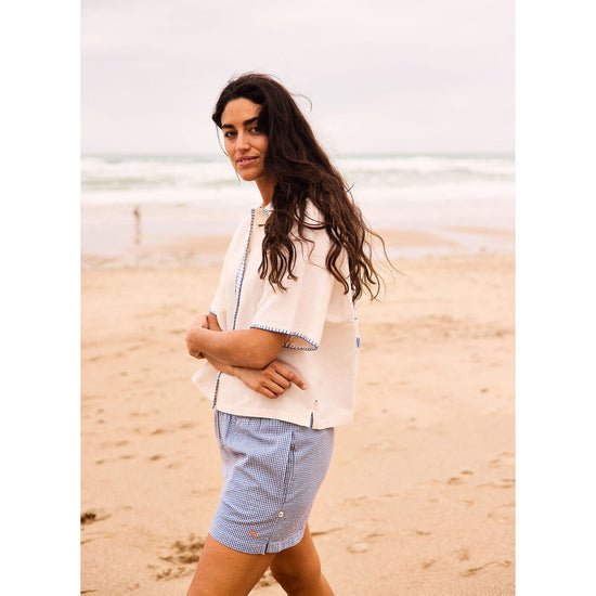 Woman standing on a beach wearing a light-colored jacket and blue shorts.