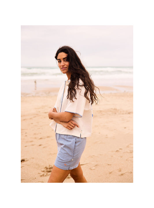 Woman standing on a beach wearing a light-colored jacket and blue shorts.