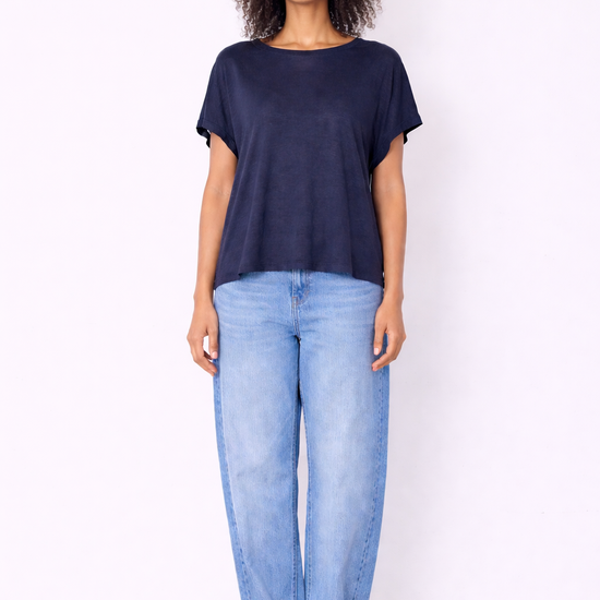 model wearing navy top and jeans on plain background 