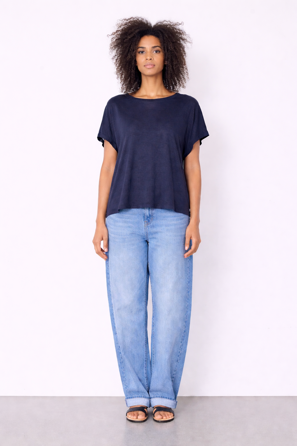 model wearing navy top and jeans on plain background 