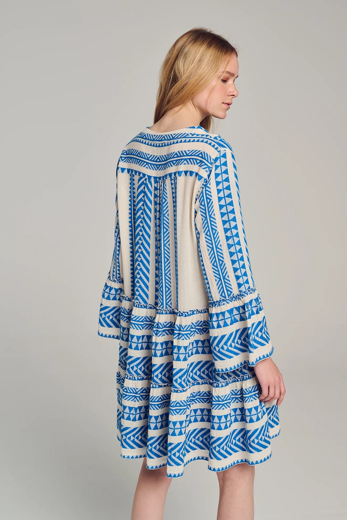 Ecru base short dress with panelled skirt and fluted bracelet length sleeves with blue geometric all over embroidery