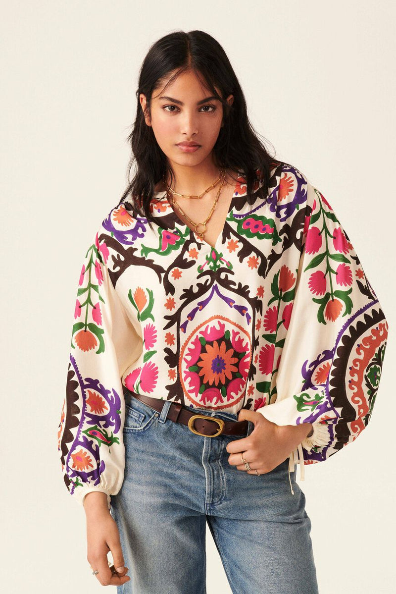 Boho inspired top with ecru base and bold all over print in pinks greens and purple. Cropped balloon sleeves with tie fastening. Henley V neckline