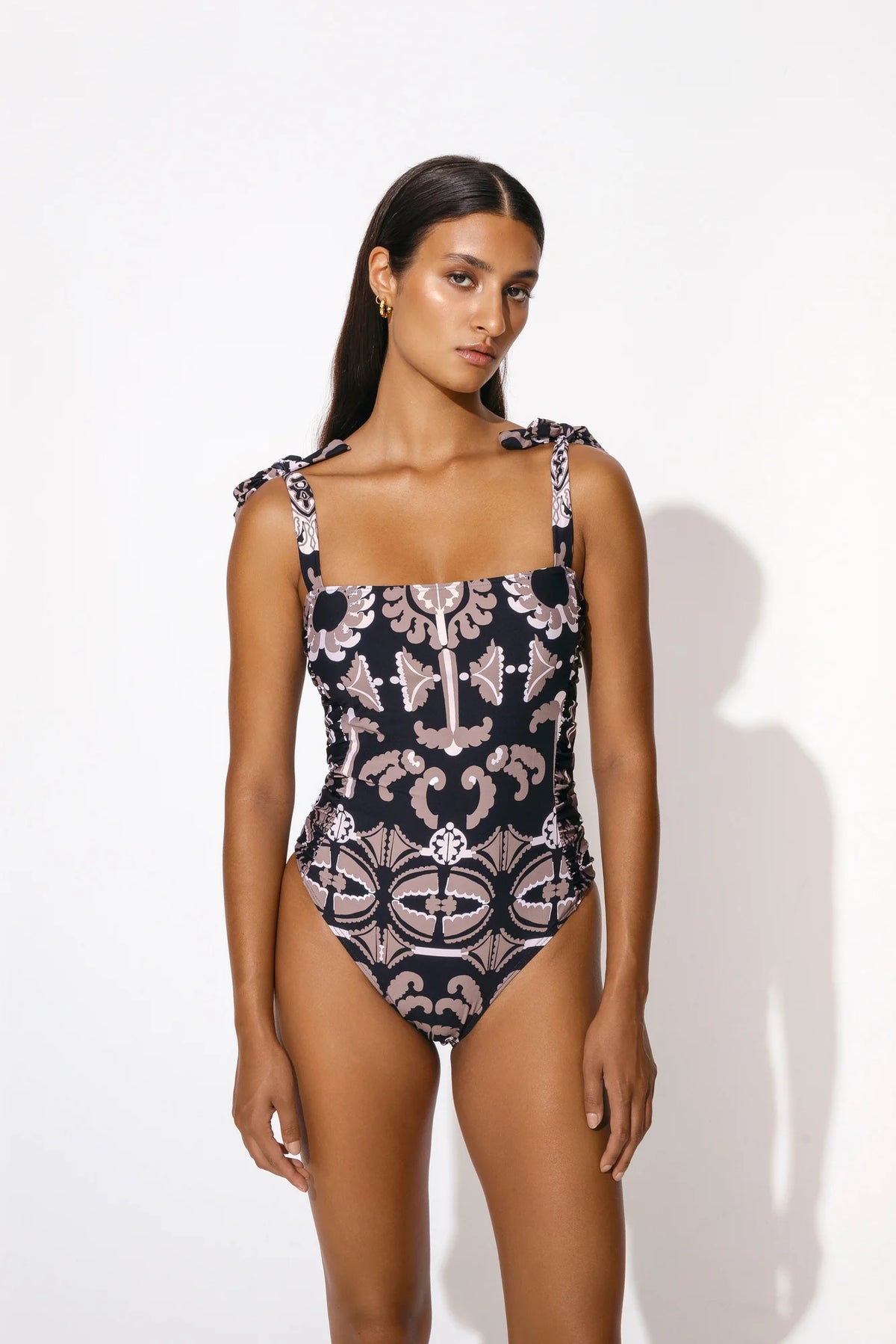 Black swimsuit with taupe and ecru motif print with high cut leg tie straps and padded cups with ruched sides