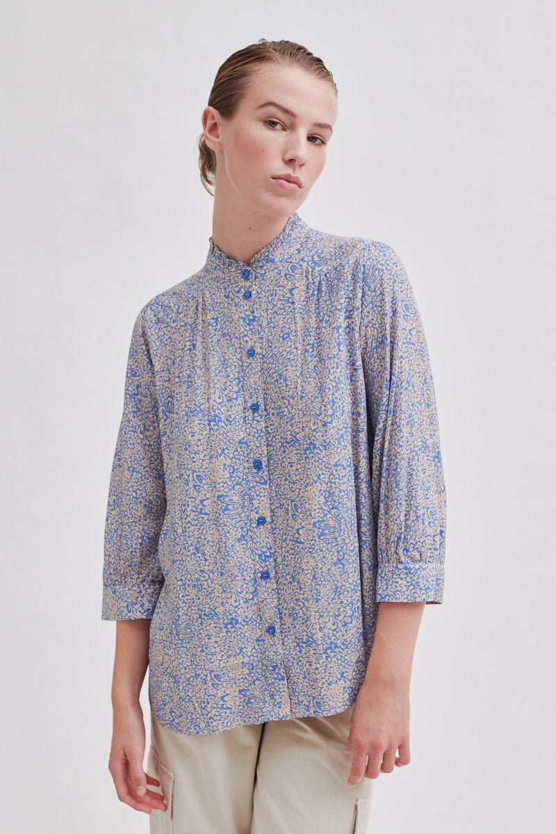 Ecru and cornflower blue ditsy floral blouse with full length placket and button fastening with grandad collar and ruffle detail with three quarter length sleeves