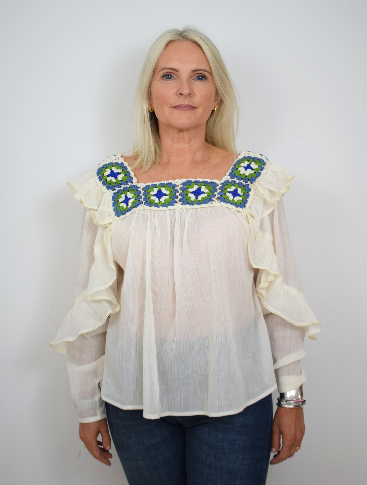 Ecru blouse with green and blue crocheted details around the square collar with ruffle details on shoulders and down arms