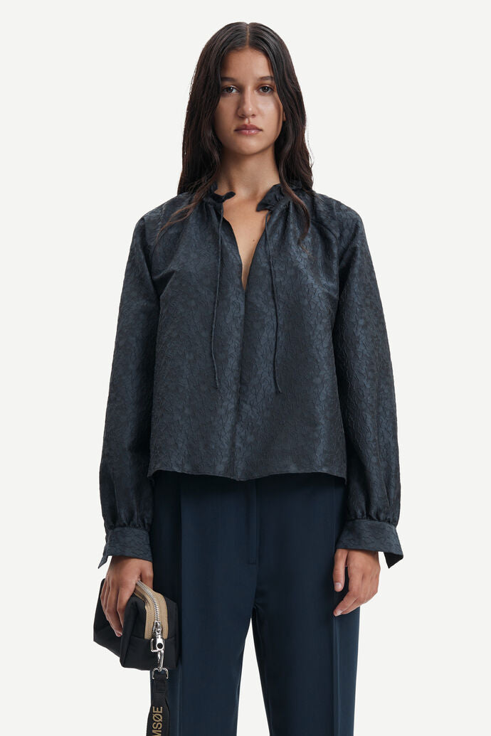 Navy tie neck blouse with long raglan sleeves in a deep navy embossed recycled polyester fabric