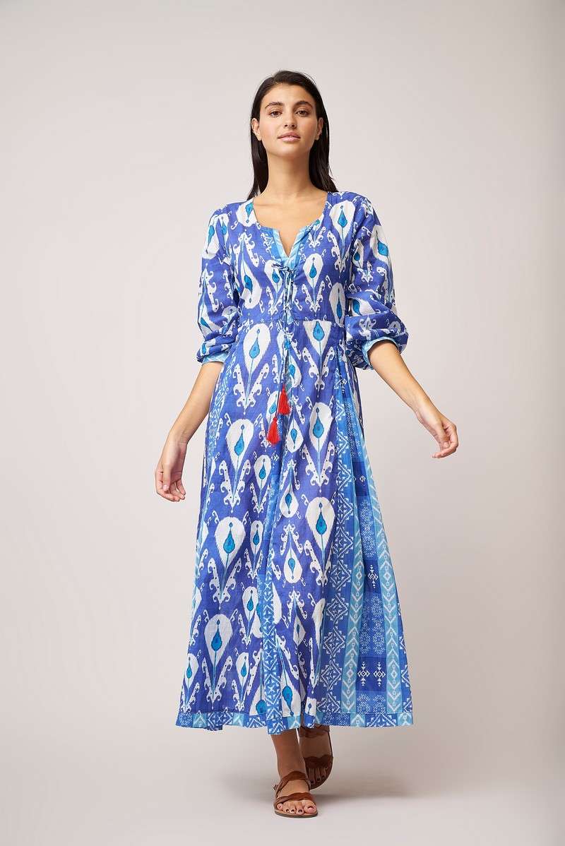 Long blue and white midi dress with three quarter length sleeves and contrasting fabric on placket, cuffs and in box pleats on the skirt with a lace tie detail on the placket with red tassles