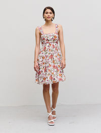 Knee length floaty summer dress with thin straps and gathering on bodice empire line in white with orange and purple floral print with purple piping detail