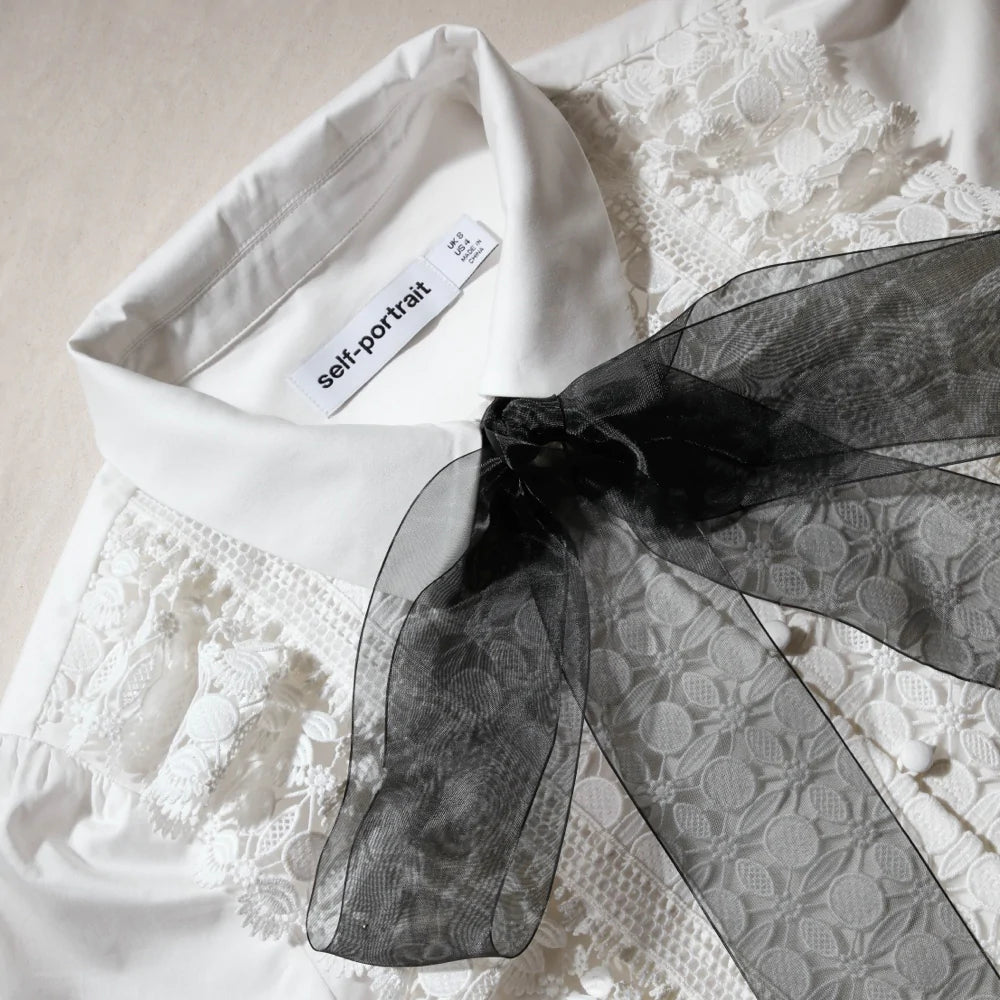 White cotton poplin shirt with classic collar lace ruffles on bodice and long sleeves with detachable black chiffon bow