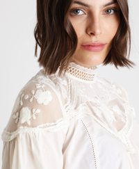 A cream blouse with lace detailing over the shoulders.